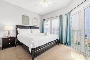 A bedroom with a bed, a nightstand, a ceiling fan, and a large window with curtains. - Six by the Ocean - Spacious 6BR Condo w/ Shared Pool and Hot Tub (Sleeps 16) (North Myrtle Beach)