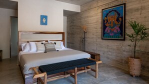 A modern bedroom with a large bed, a bench, a potted plant, and a wall-mounted artwork.
