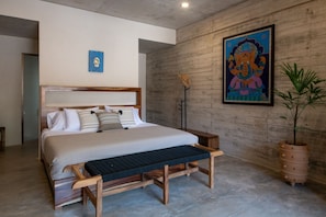 A modern bedroom with a large bed, a bench, a potted plant, and a wall-mounted artwork.