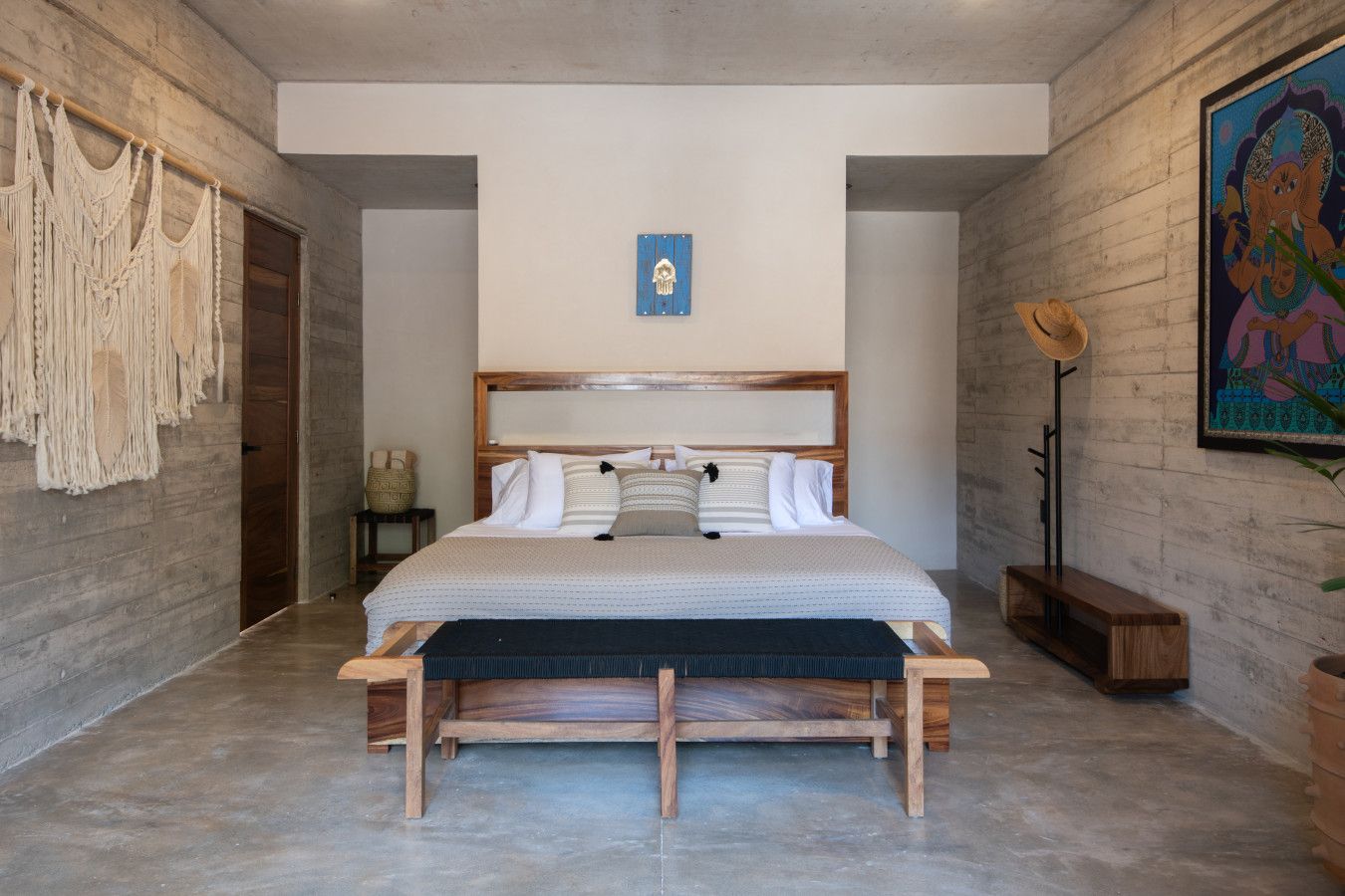 Une chambre à coucher avec un lit en bois, une tête de lit, une œuvre d’art accrochée au mur et une décoration murale en macramé.