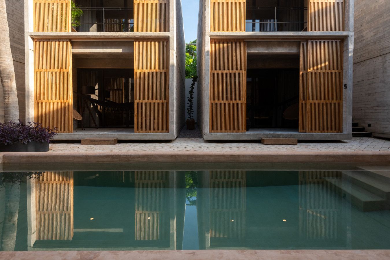 Un edificio moderno con due grandi porte scorrevoli in legno, una piscina sullo sfondo e un cielo sereno.