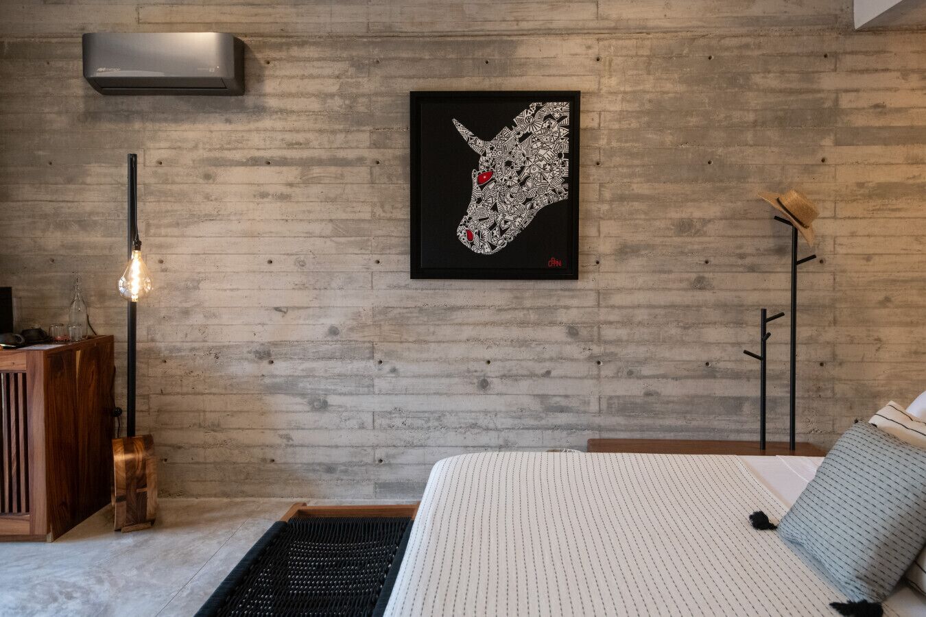 Une chambre à coucher comprenant un lit, un climatiseur fixé au mur, une lampe sur pied et une œuvre d’art encadrée.