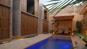 Un espace piscine avec une piscine bleue, des clôtures en bois et un coin salon comprenant des chaises et des plantes.