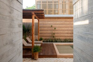 A modern outdoor patio with a wooden deck, lounge chairs, a small pool, and a bamboo wall.