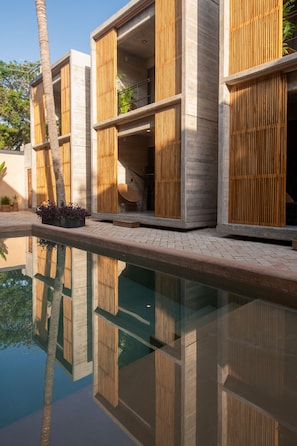 A modern building with a pool, wooden slatted walls, and a clear reflection in the water.