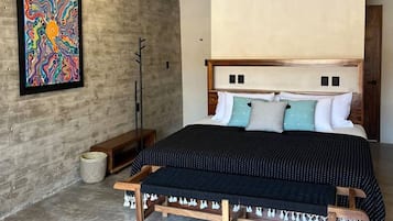 Een slaapkamer met een bed, een plafondventilator, een geweven lamp en een kleurrijk abstract schilderij aan de muur.
