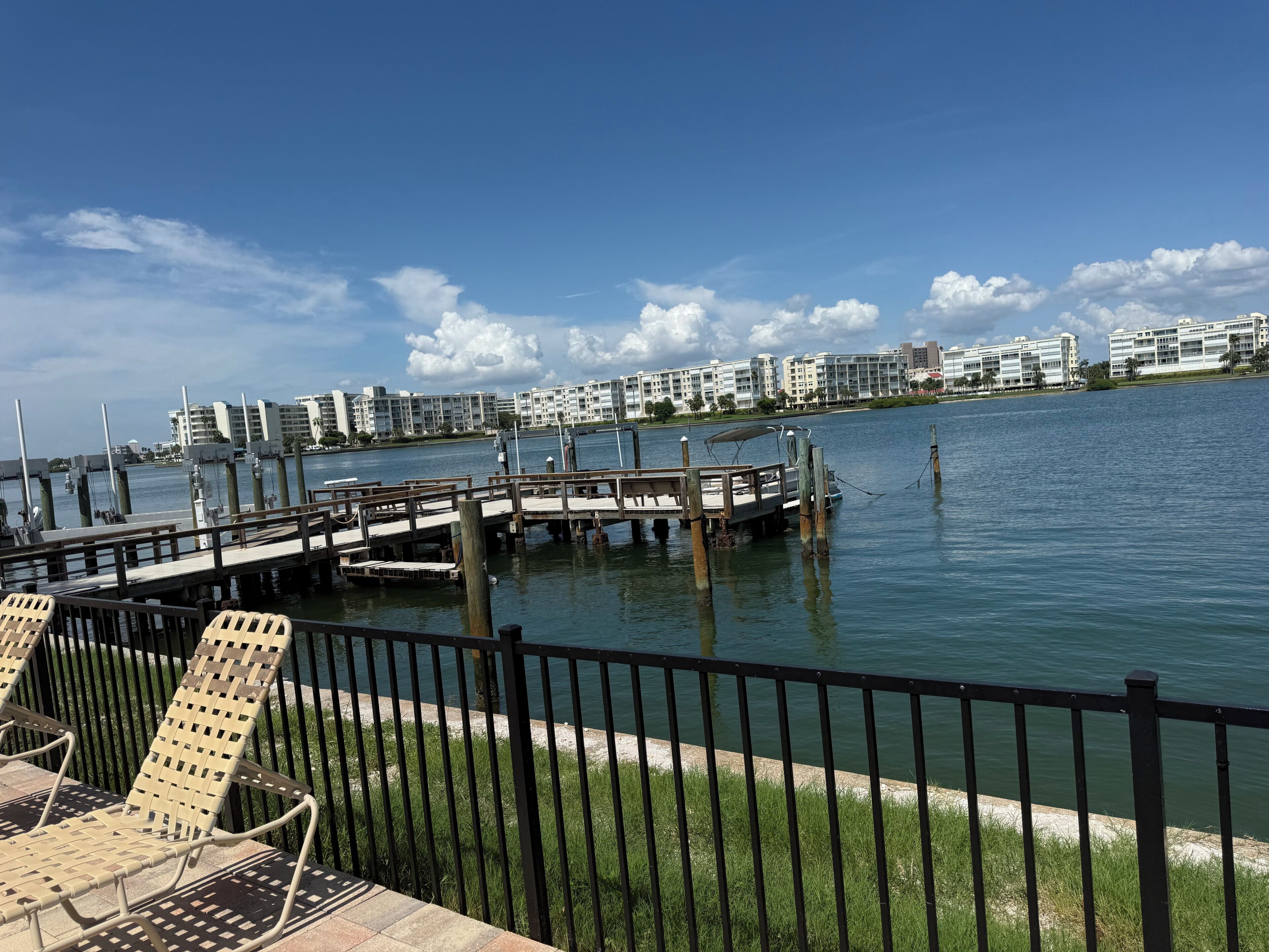 A waterfront view with a dock, chairs, and buildings in the background.