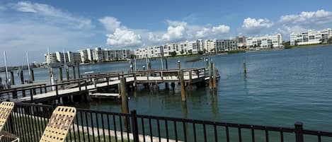 A waterfront view with a dock, chairs, and buildings in the background.