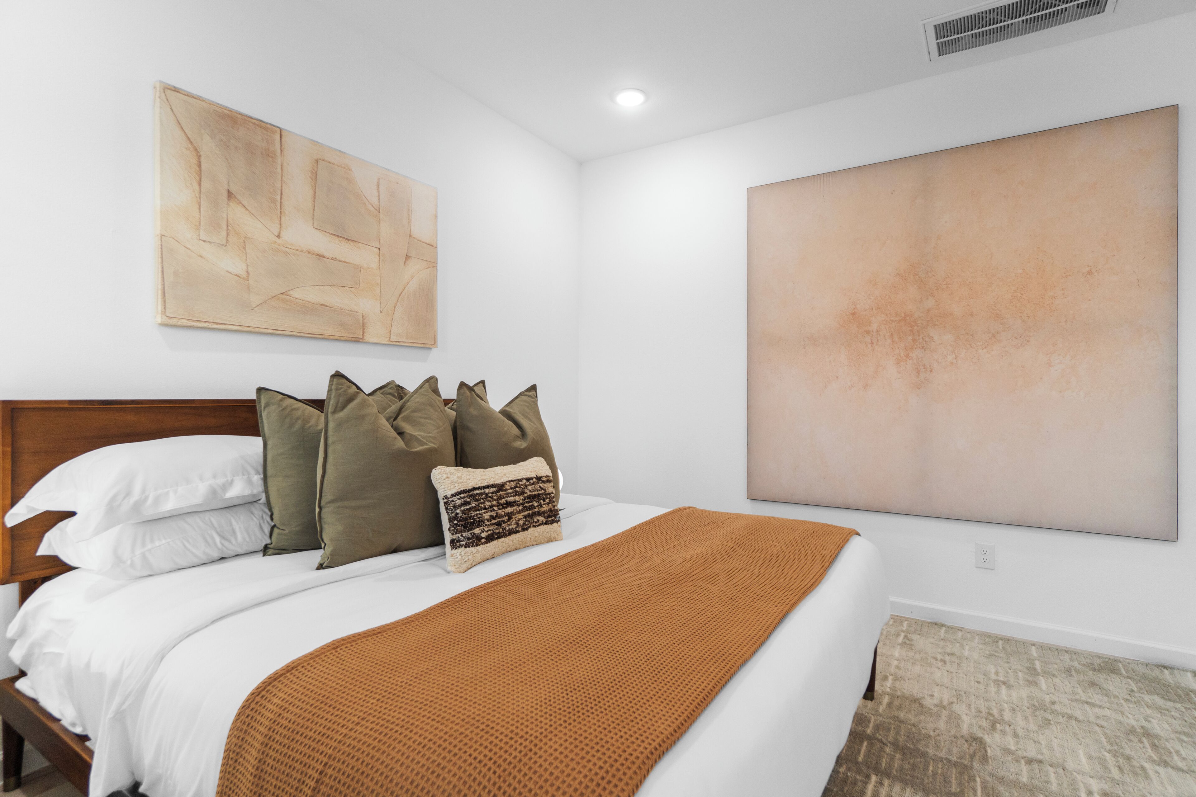 A hotel room with a bed, pillows, a blanket, a large abstract painting, and a large textured wall.
