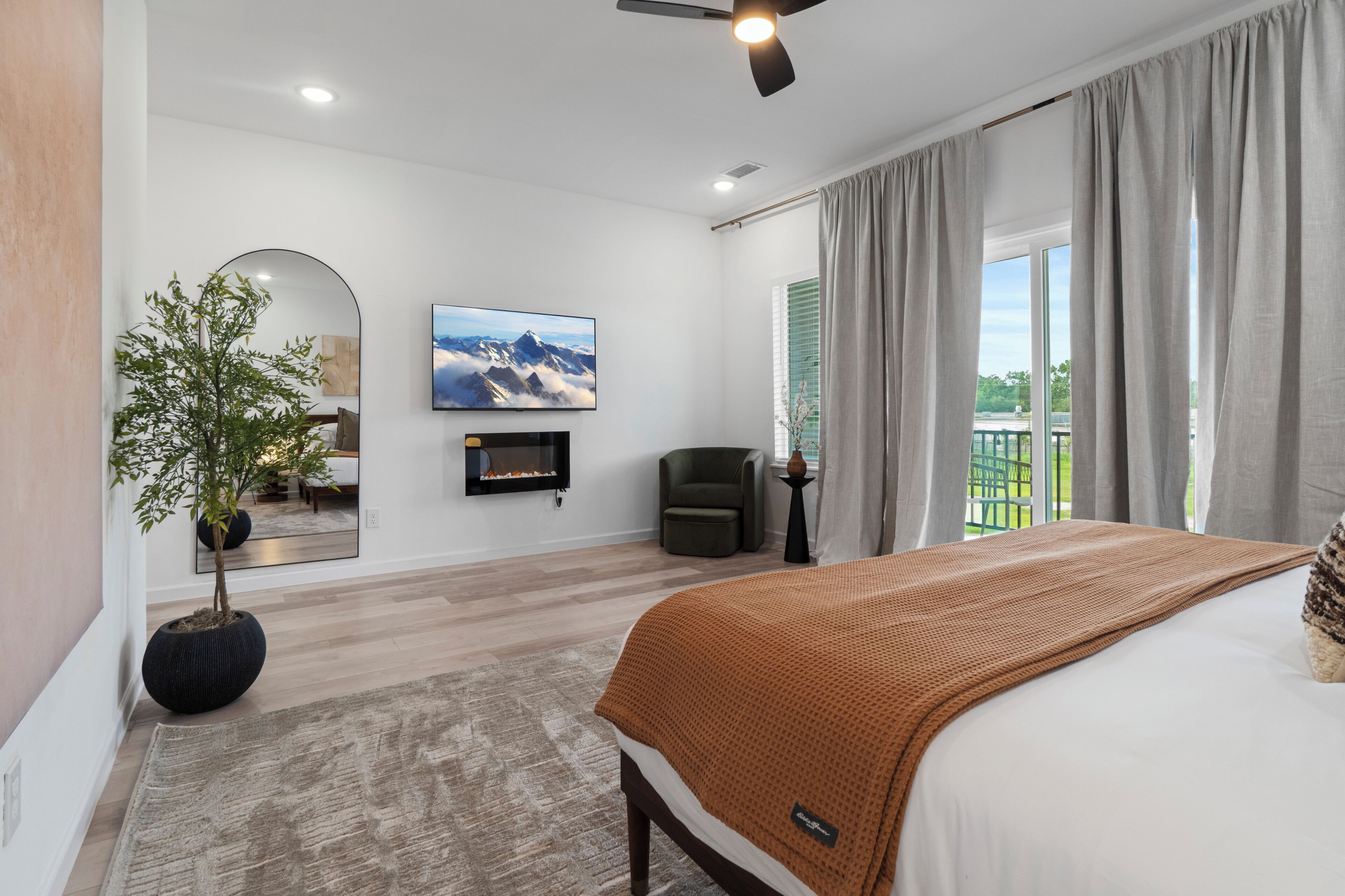 A modern bedroom with a bed, a television, a fireplace, and a view of the outdoors.