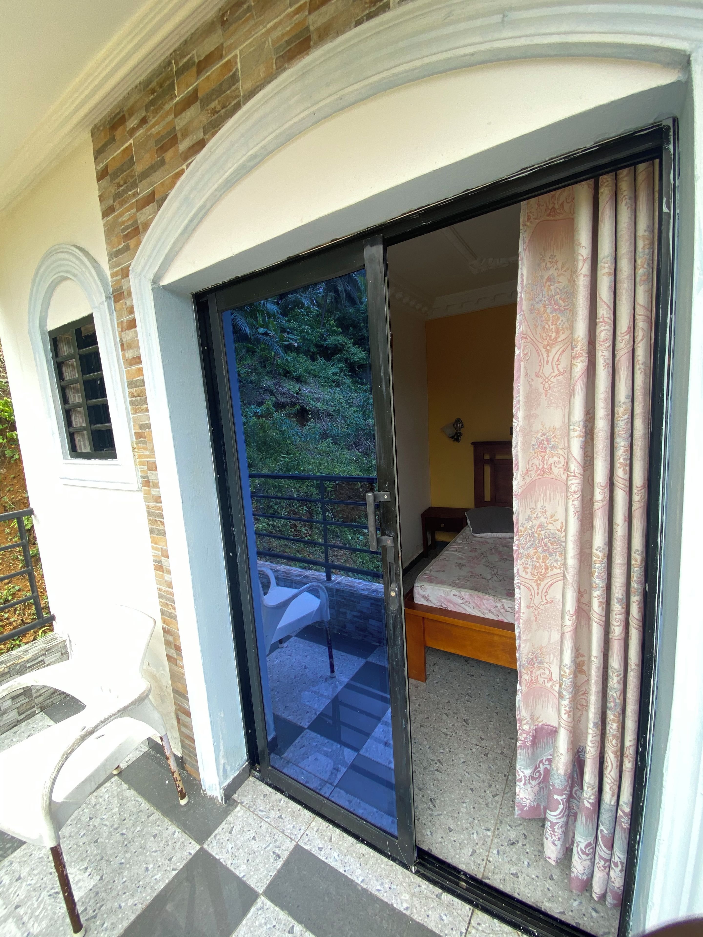 Quarto com cama, uma cadeira e vista para o verde através de uma porta de correr de vidro.