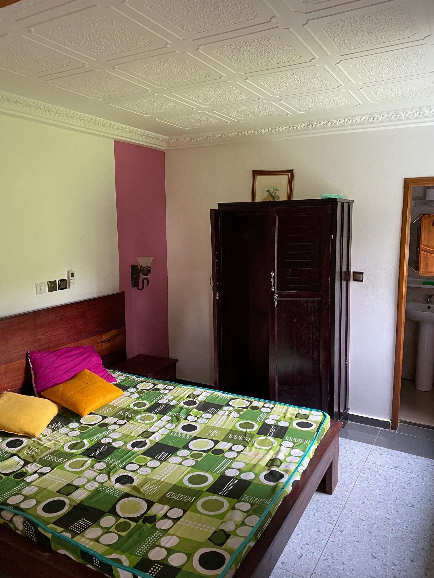 A bedroom with a bed, a wardrobe, a wall-mounted light, and a door leading to a bathroom.