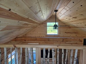 Un intérieur en bois avec un plafond en pente, une fenêtre et un ventilateur de plafond.