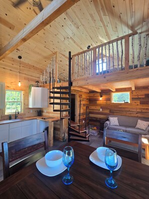 A wooden interior with a dining table, chairs, a sofa, and a staircase. - Peaceful 1-bedroom cabin for a cozy stay (Sandstone)