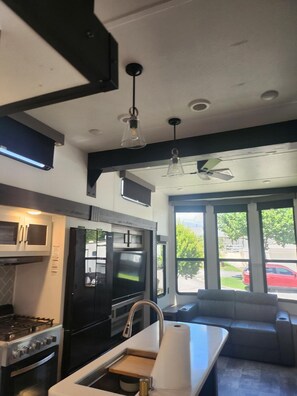 A modern kitchen with a gas stove, oven, microwave, and a built-in TV. There is a seating area with a sofa and a window providing a view of the outdoors. - Gregerson's Getaway at River Rock Landing (Gadsden)