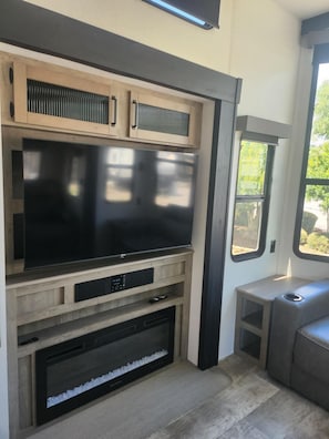 A compact living space with a large flat-screen TV, built-in entertainment unit, and a small seating area. - Gregerson's Getaway at River Rock Landing (Gadsden)