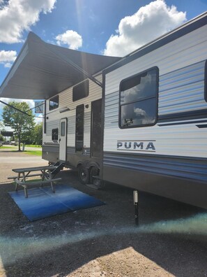 A PUMA RV with an attached awning, a picnic table, and a blue mat on the ground. - Gregerson's Getaway at River Rock Landing (Gadsden)