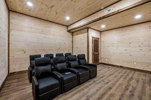 Ein Zimmer mit Holzwänden und -decke, ausgestattet mit schwarzen Massagesesseln, die in einer Reihe angeordnet sind.