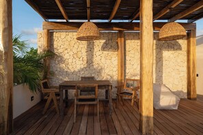 Eine Terrasse im Freien mit einer Steinsäule, Holzmöbeln und gewobenen Hängeleuchten.