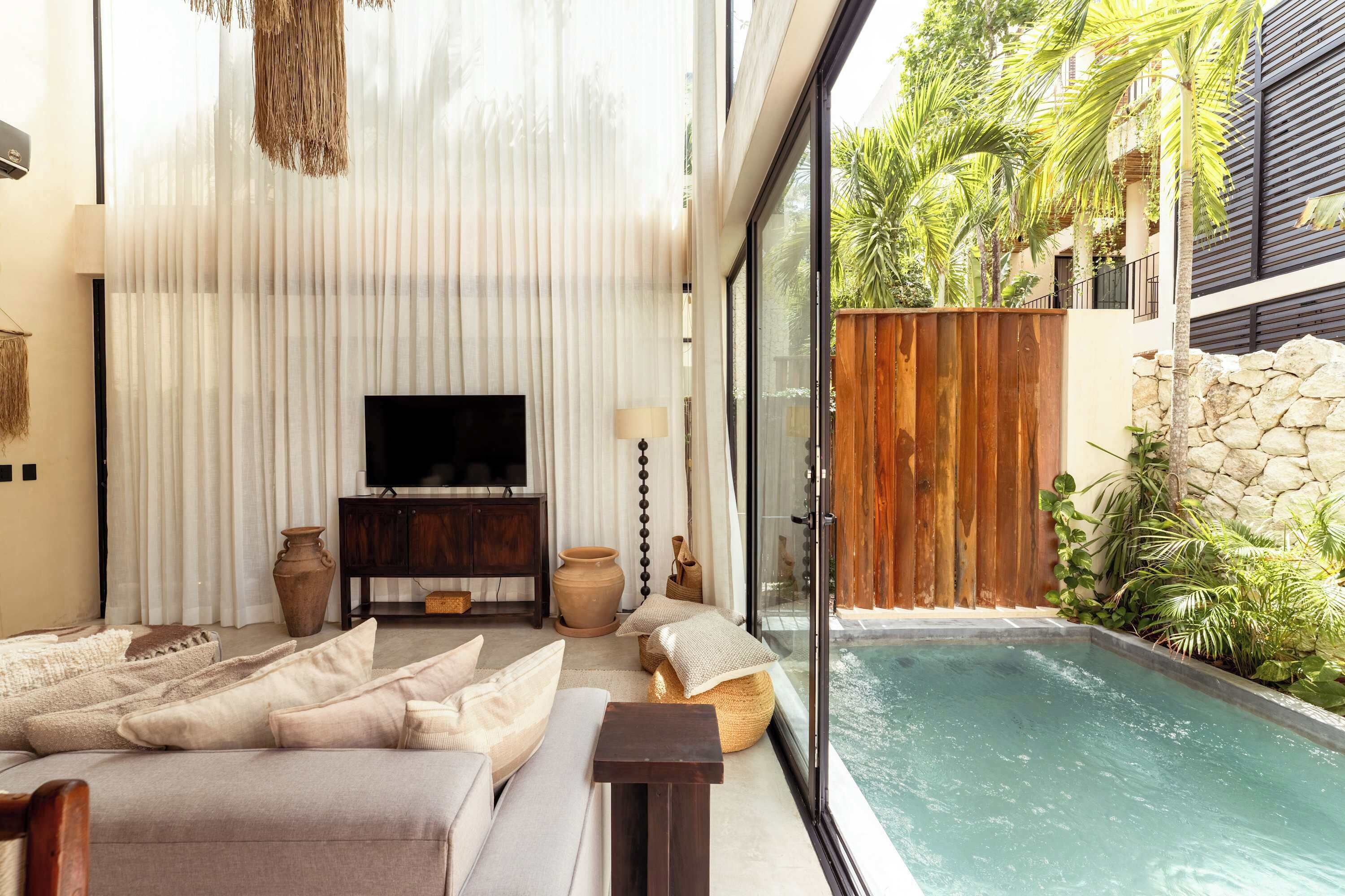 A modern living room with a sofa, TV, and decorative items, overlooking a private pool and lush greenery.
