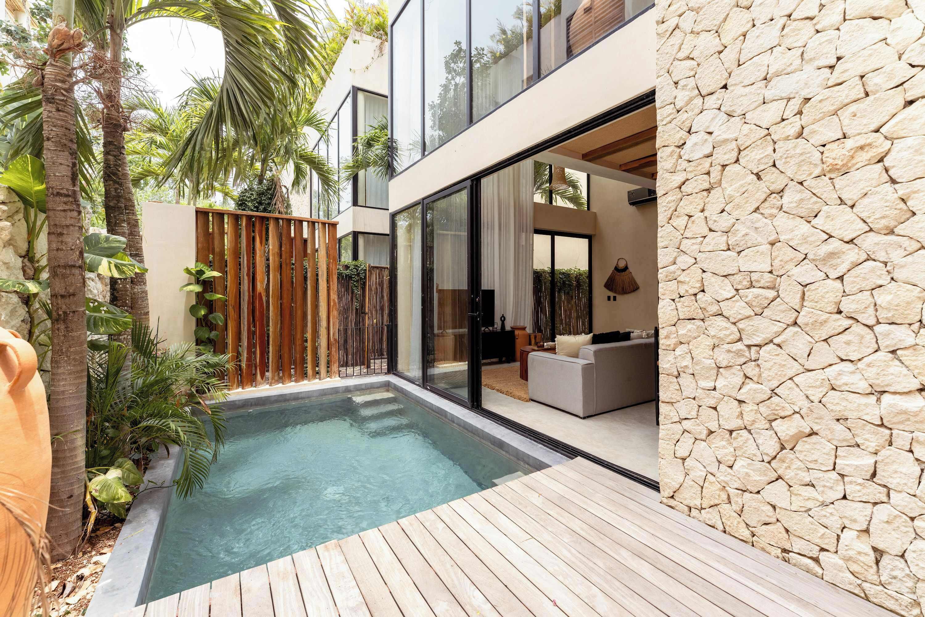 Ein moderner Poolbereich im Freien mit einer Holzterrasse, einer Steinmauer und einem gläsernen Wohnbereich.