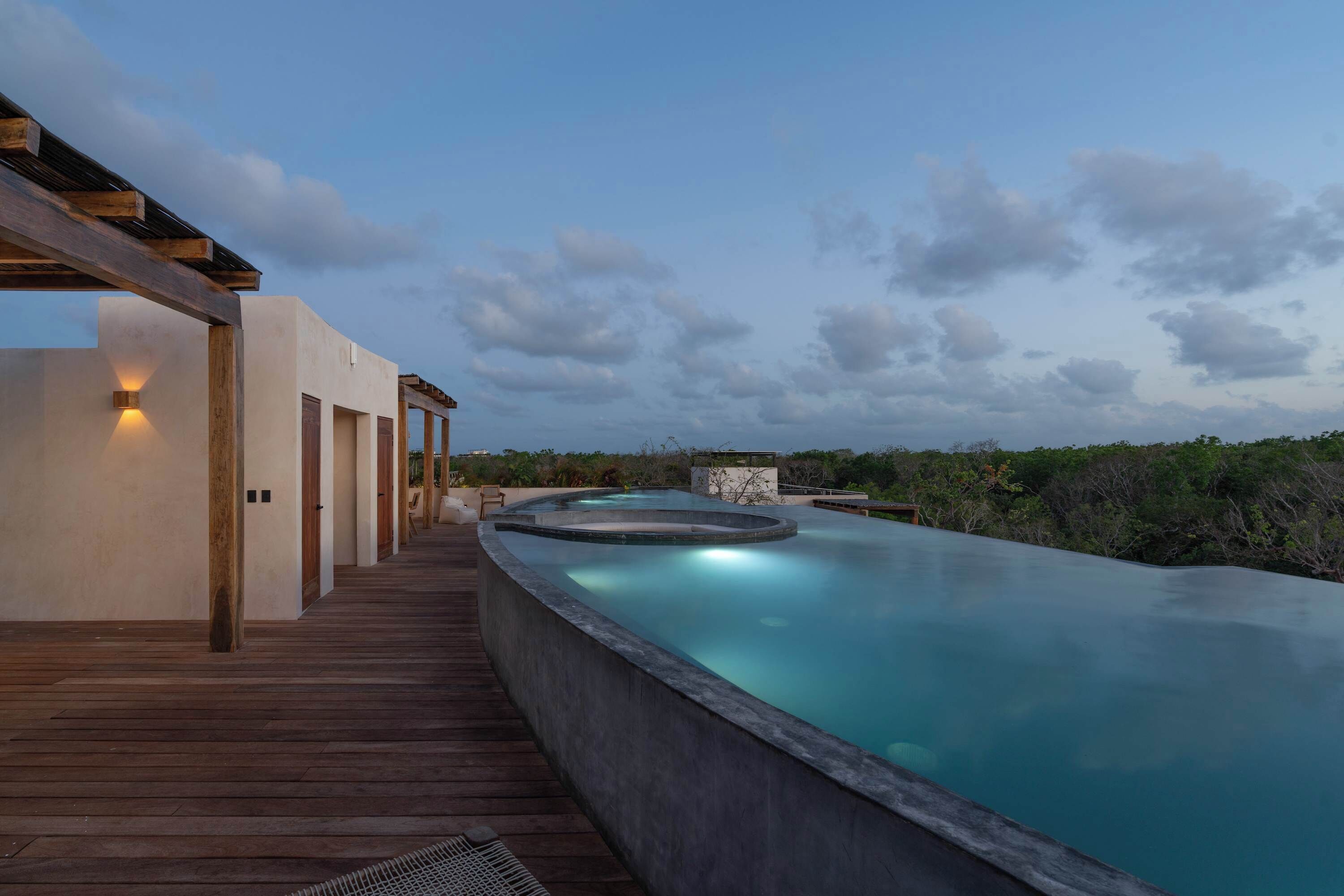 Ein Pool mit Holzterrasse und einem Gebäude mit beleuchteter Seite.