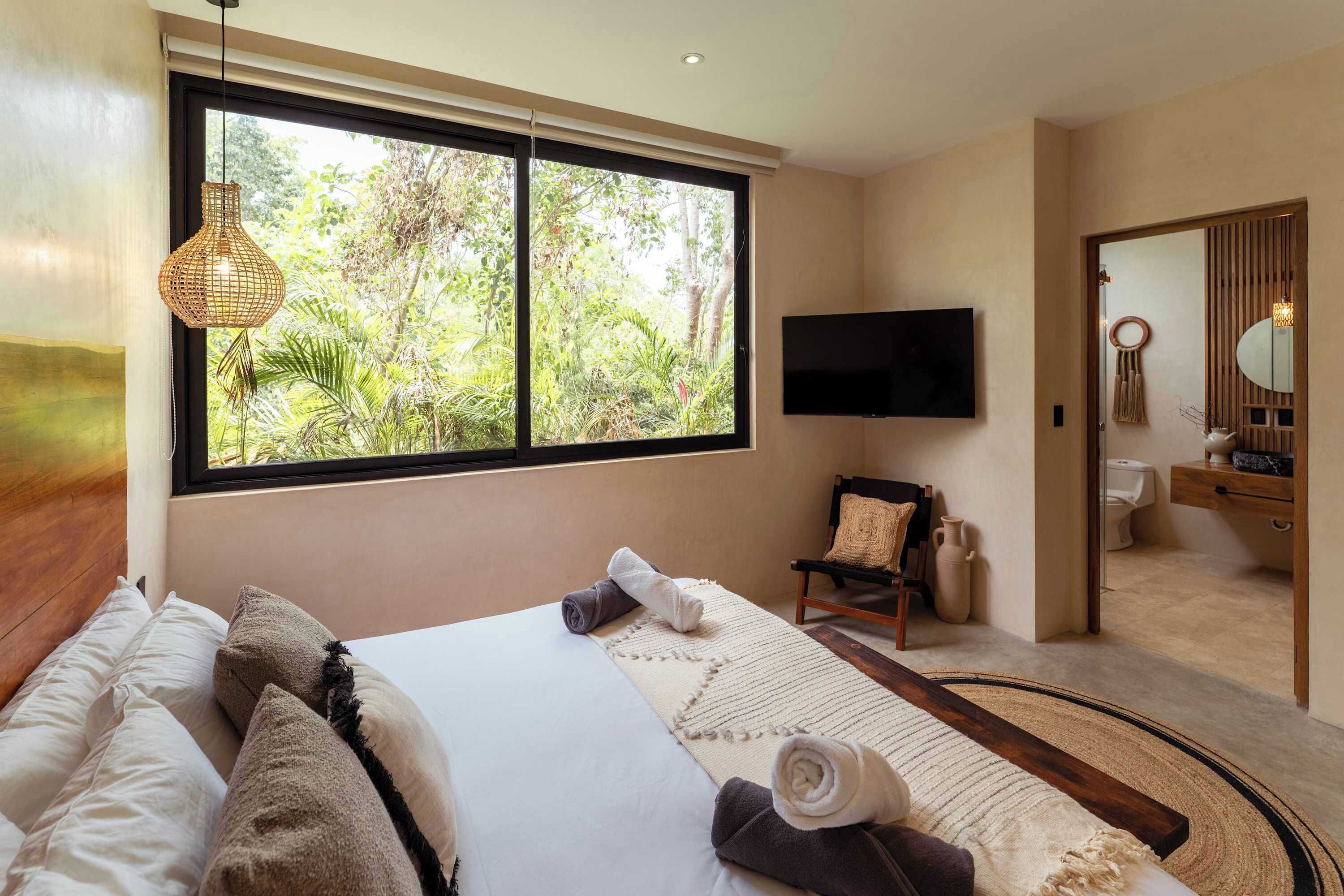 Ein modernes Schlafzimmer mit großem Fenster, einem Bett mit weißen Leinen, einem Holz-Kopfteil und Blick auf Grünfläche.