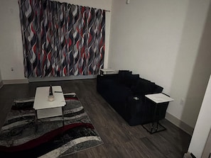 Een woonkamer met een donkergrijze bank, een witte salontafel en een vloerkleed met dessin.