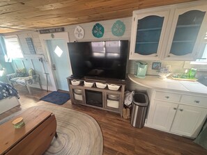 A cozy living room with a flat-screen TV, wooden cabinets, and a cozy chair. - Quaint 1-bedroom studio with AC in Oak Island - just a 1/2 mile to the beach! (Oak Island)
