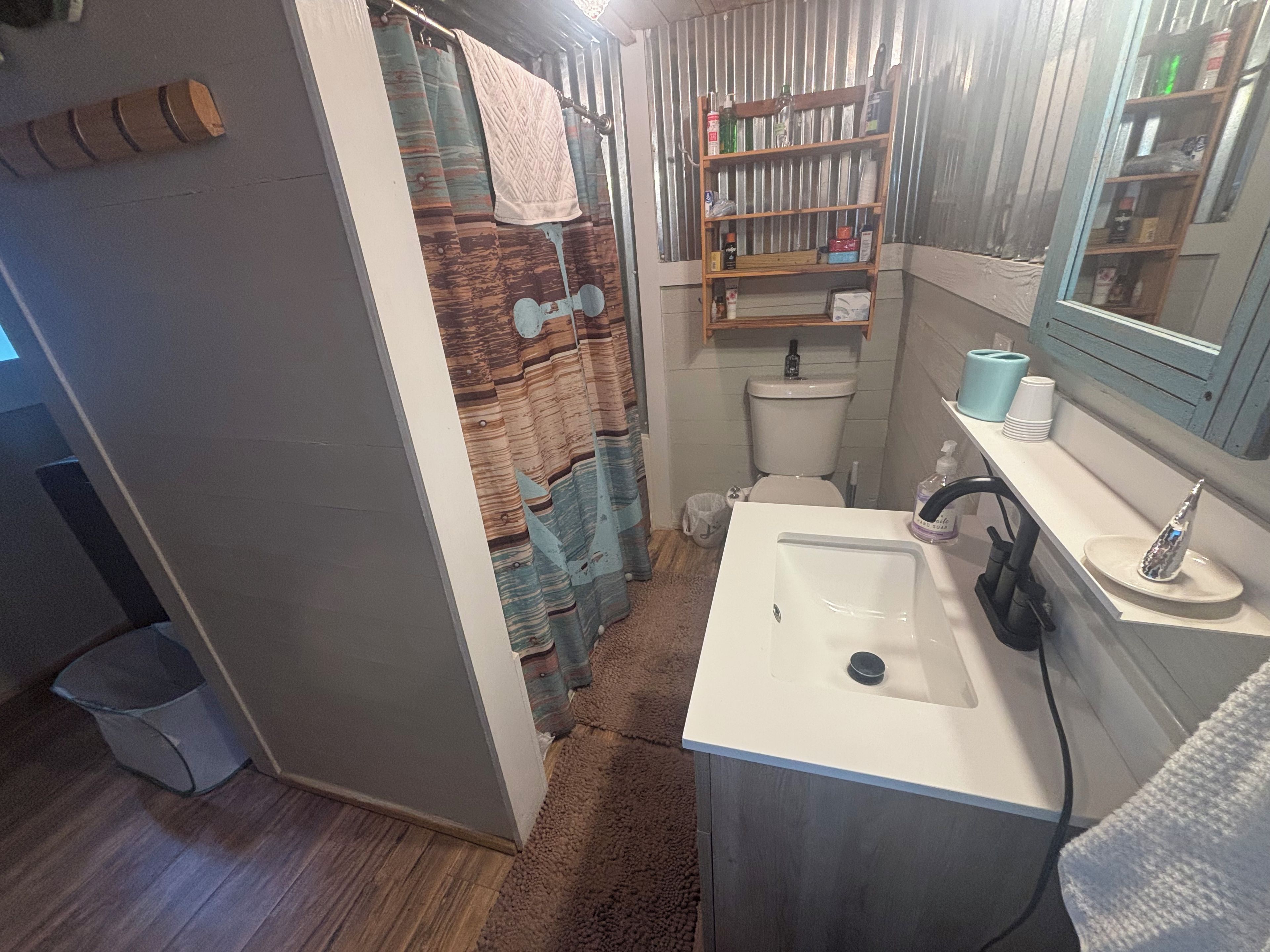 A bathroom with a shower curtain, toilet, sink, and shelves with toiletries.