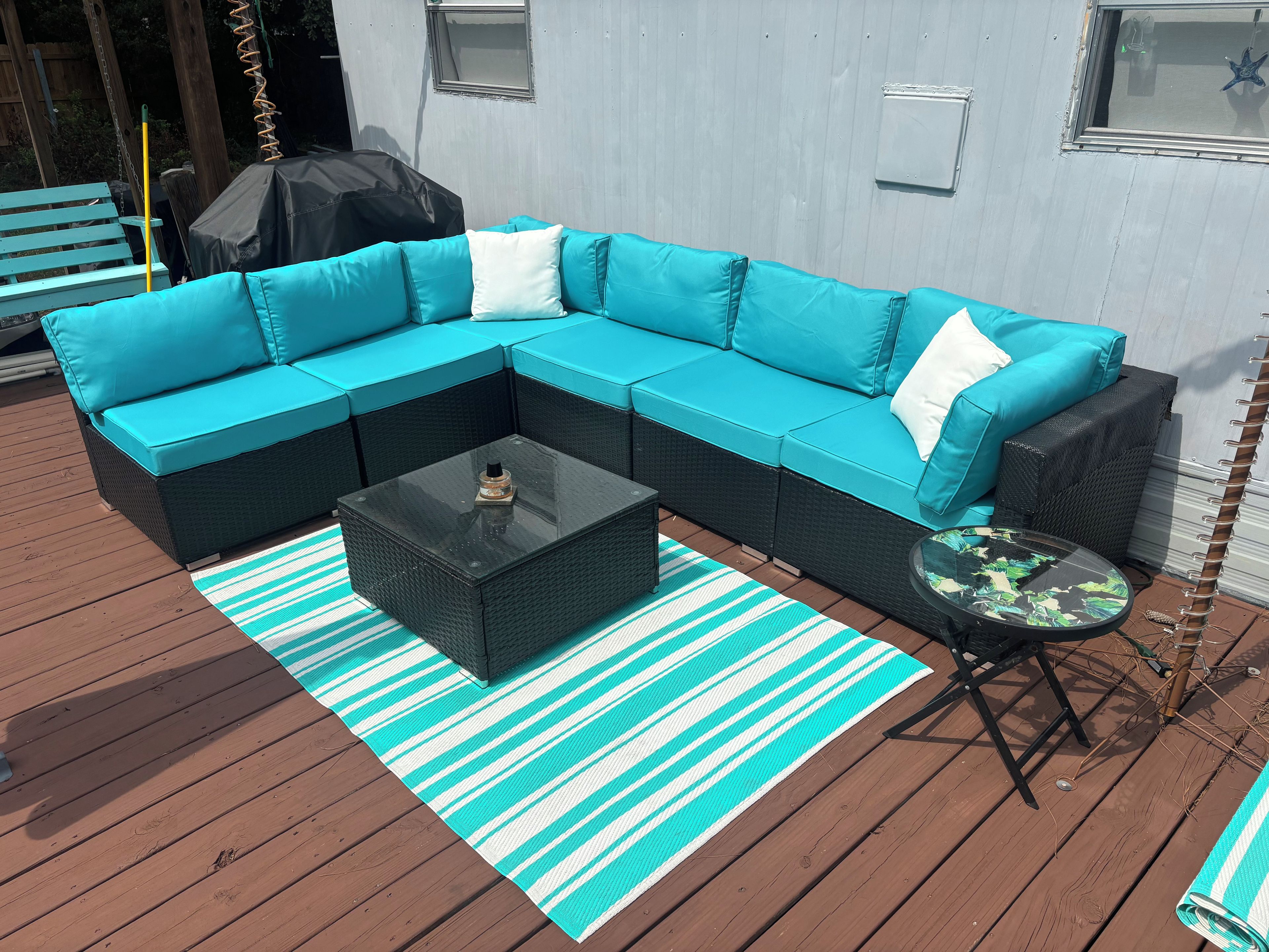 Un canapé modulable avec des coussins, une table basse et un tapis à rayures sur une terrasse en bois.