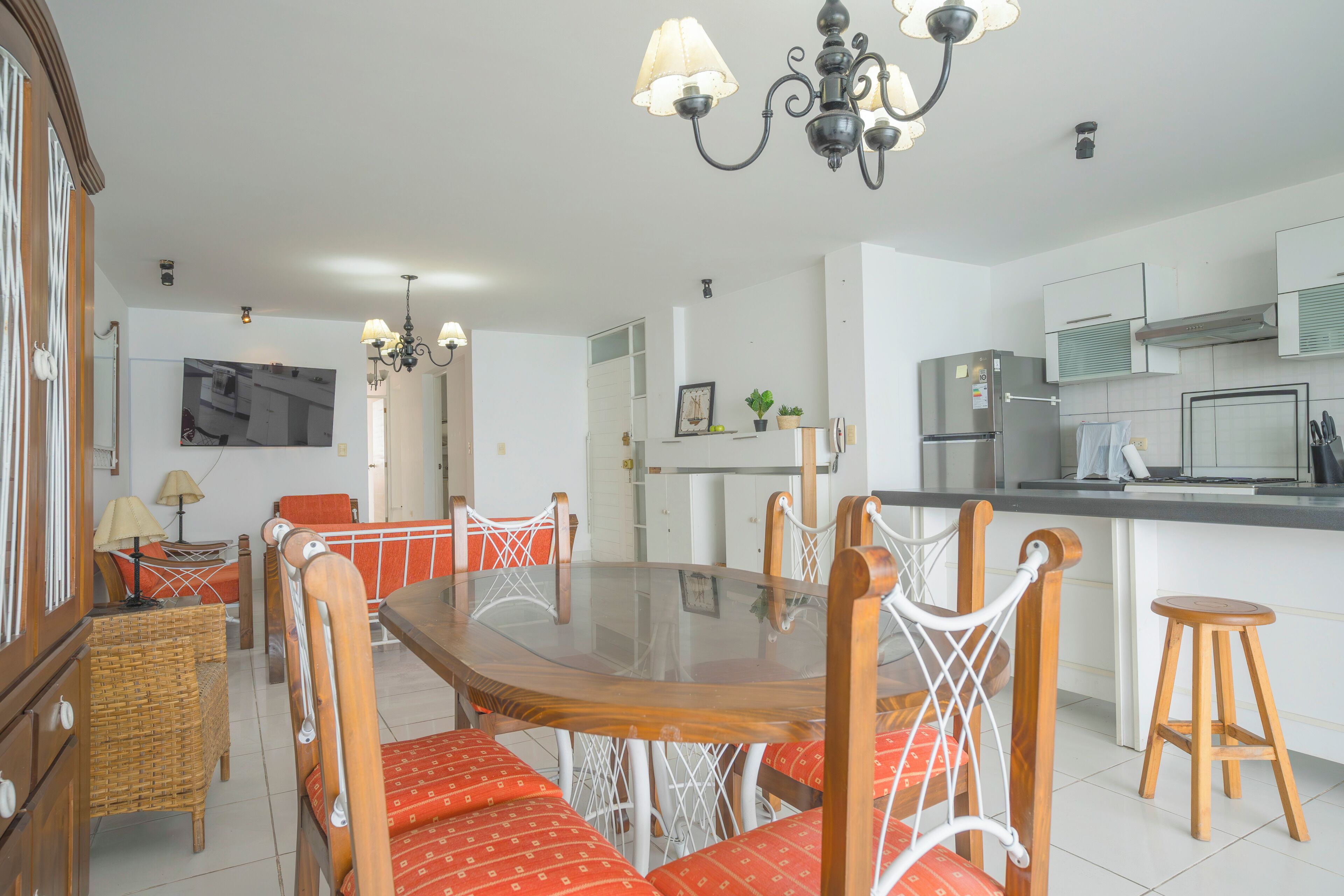 A modern kitchen with a dining area, featuring a wooden table with red upholstered chairs, a chandelier, and a refrigerator.
