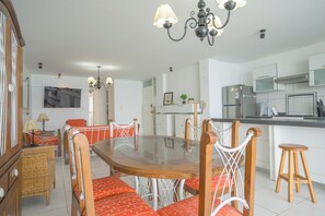 A modern kitchen with a dining area, featuring a wooden table with red upholstered chairs, a chandelier, and a refrigerator.