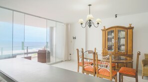 A dining area with a view of the ocean, a chandelier, and a wooden cabinet.