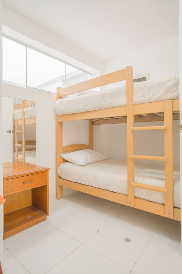A bunk bed with a wooden frame, a bedside table, and a mirror.