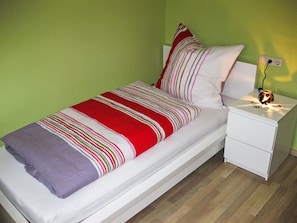 Ein Zimmer mit einem Einzelbett, einem weißen Nachttisch, einem Beistelltisch, grünen Wänden und einer Streifen-Decke.