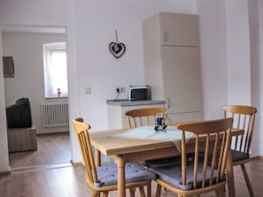 A dining area with a wooden table and four chairs, a small kitchen area with a microwave, and a heart-shaped decoration on the wall. - Ferienwohnung Debacher by Interhome (Rust)