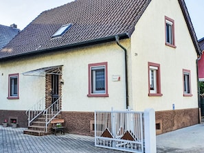 A two-story building with a tiled roof, a staircase leading to the entrance, and a gated driveway. - Ferienwohnung Debacher by Interhome (Rust)