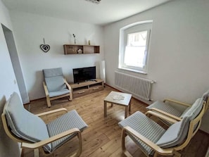 Una sala de estar con televisor, sofá, mesa de centro y ventana.
