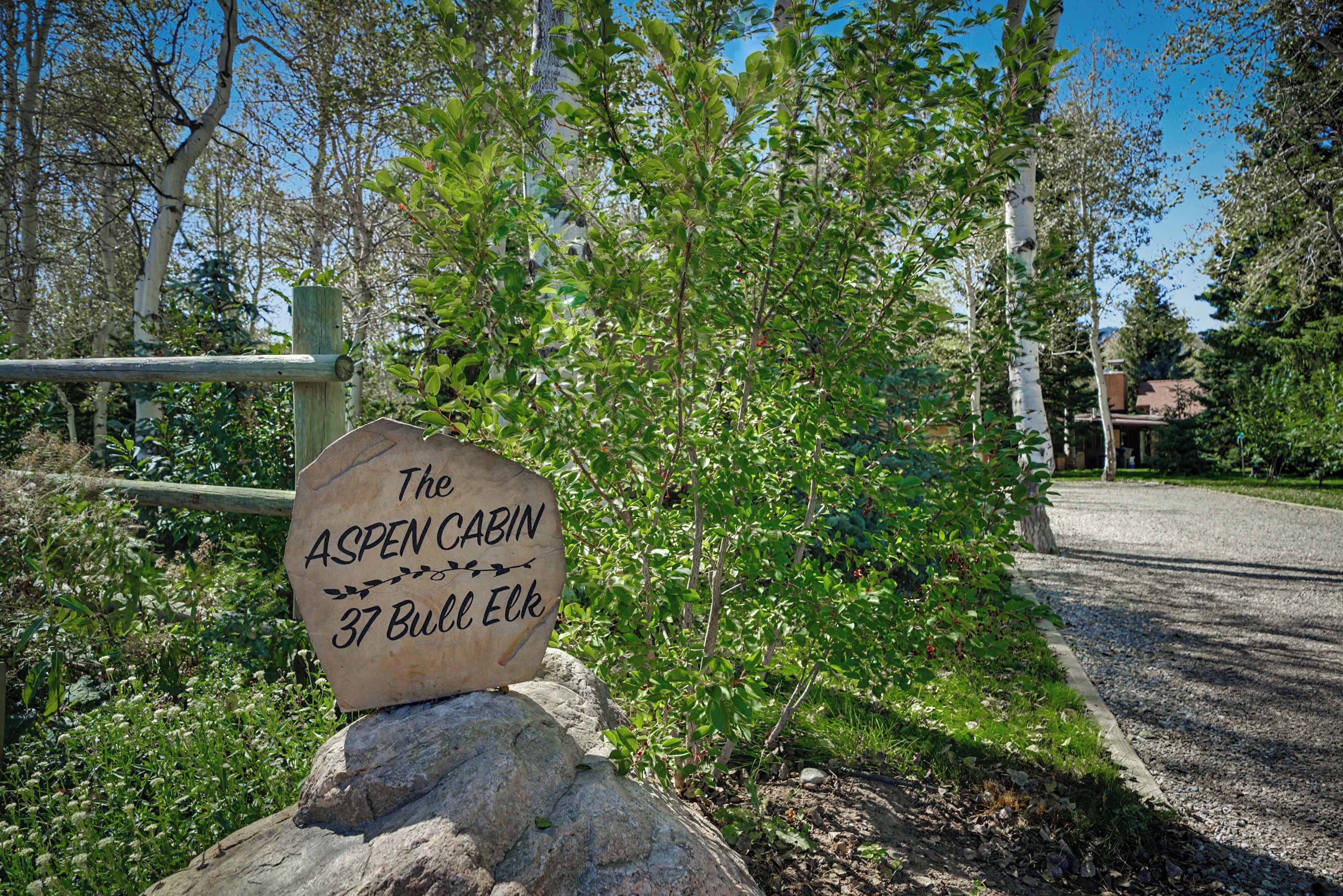 A wooden sign with the text 'The Aspen Cabin 37 Bull Elk' on a rock.