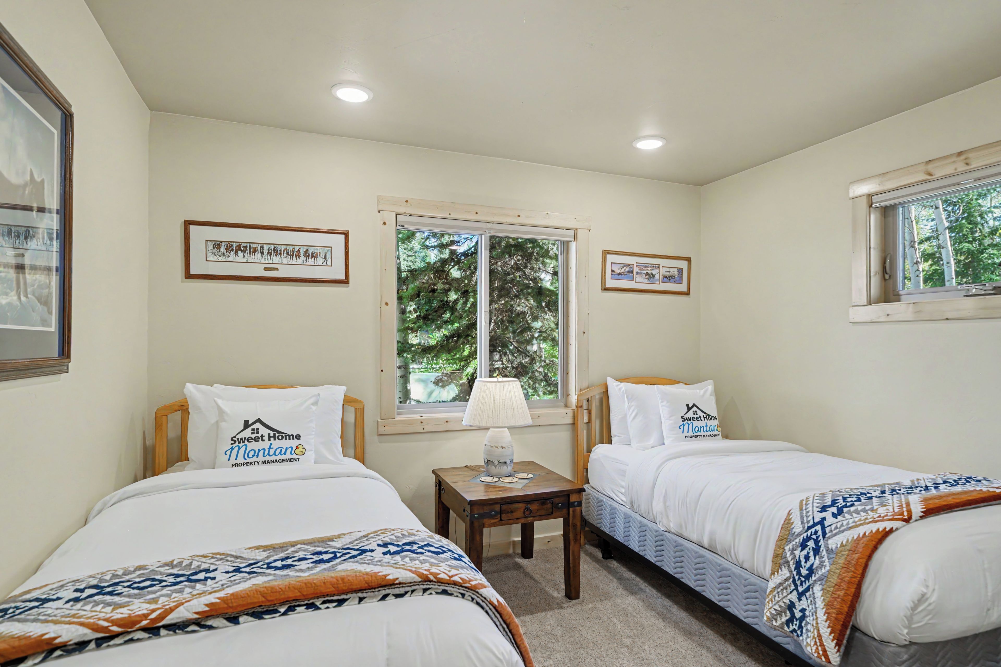 A bedroom with two beds, a window with a view of trees, and wall-mounted artwork.