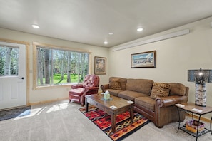 A living room with a large window, a leather armchair, a brown sofa, a coffee table, and a lamp. - 7 minutes to Yellowstone The Aspen Cabin (West Yellowstone)