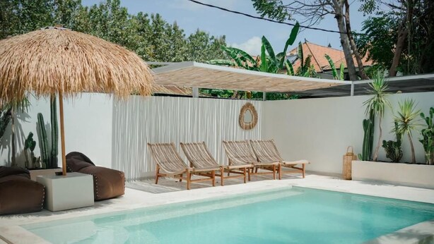 Une piscine avec des chaises longues et un parasol en chaume.