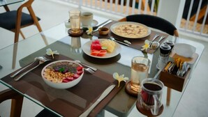 Une table à manger dressée pour le petit-déjeuner, avec un bol de céréales, une assiette de fruits, une tasse de café et un verre d’eau.