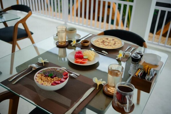 A dining table with a breakfast setting including a bowl of cereal, a plate of fruit, a cup of coffee, and a glass of water. - Lumbung Asmara (Buleleng)