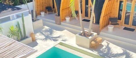 A pool area with a thatched umbrella, wooden structures, and palm trees.