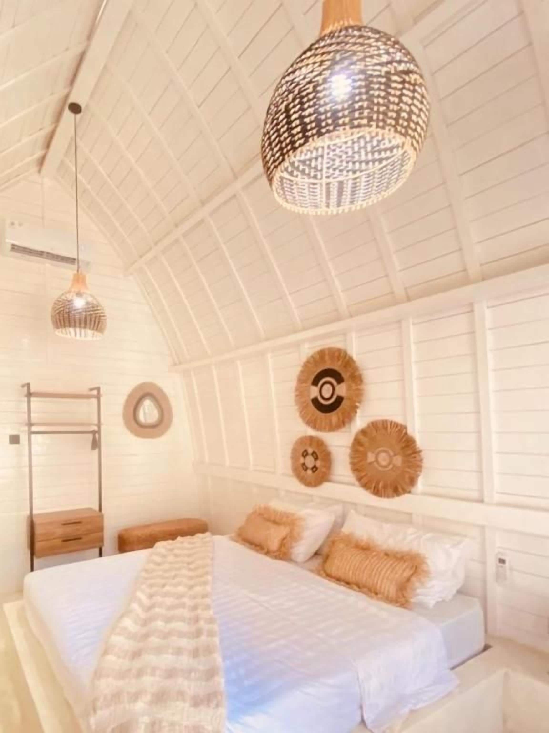 A bedroom with a large bed, a hanging light fixture, and wall decor.