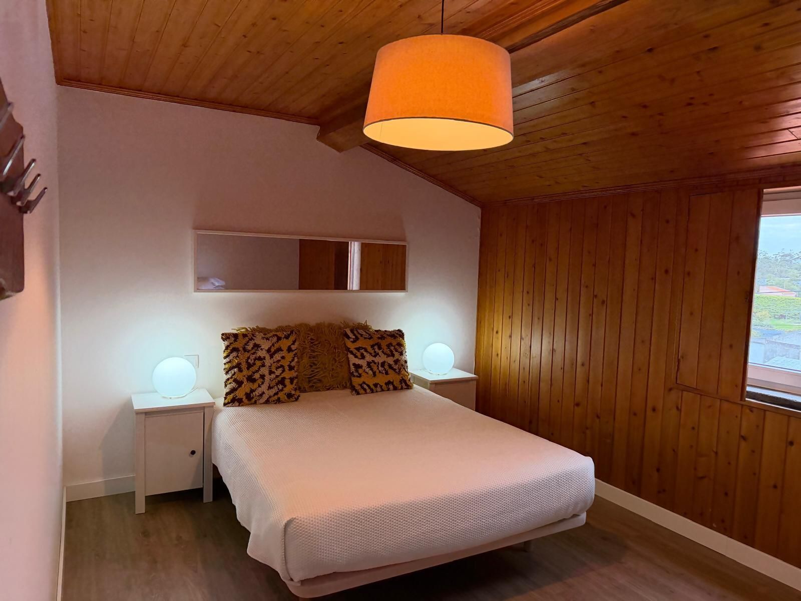 Et soveværelse med seng, trævægge, en loftlampe og et natbord med lampe.
