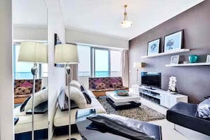 A modern living room with a sofa, coffee table, TV, and a view of the ocean. - Luxury 1BR Ocean Heights, 64th Floor Panoramic Sea and Palm Views with Jacuzzi (Dubai)
