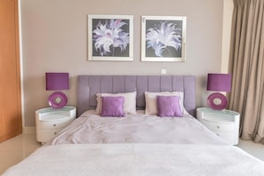 A bedroom with a bed, two nightstands, two lamps, and two framed floral artworks on the wall. - Luxury 1BR Ocean Heights, 64th Floor Panoramic Sea and Palm Views with Jacuzzi (Dubai)